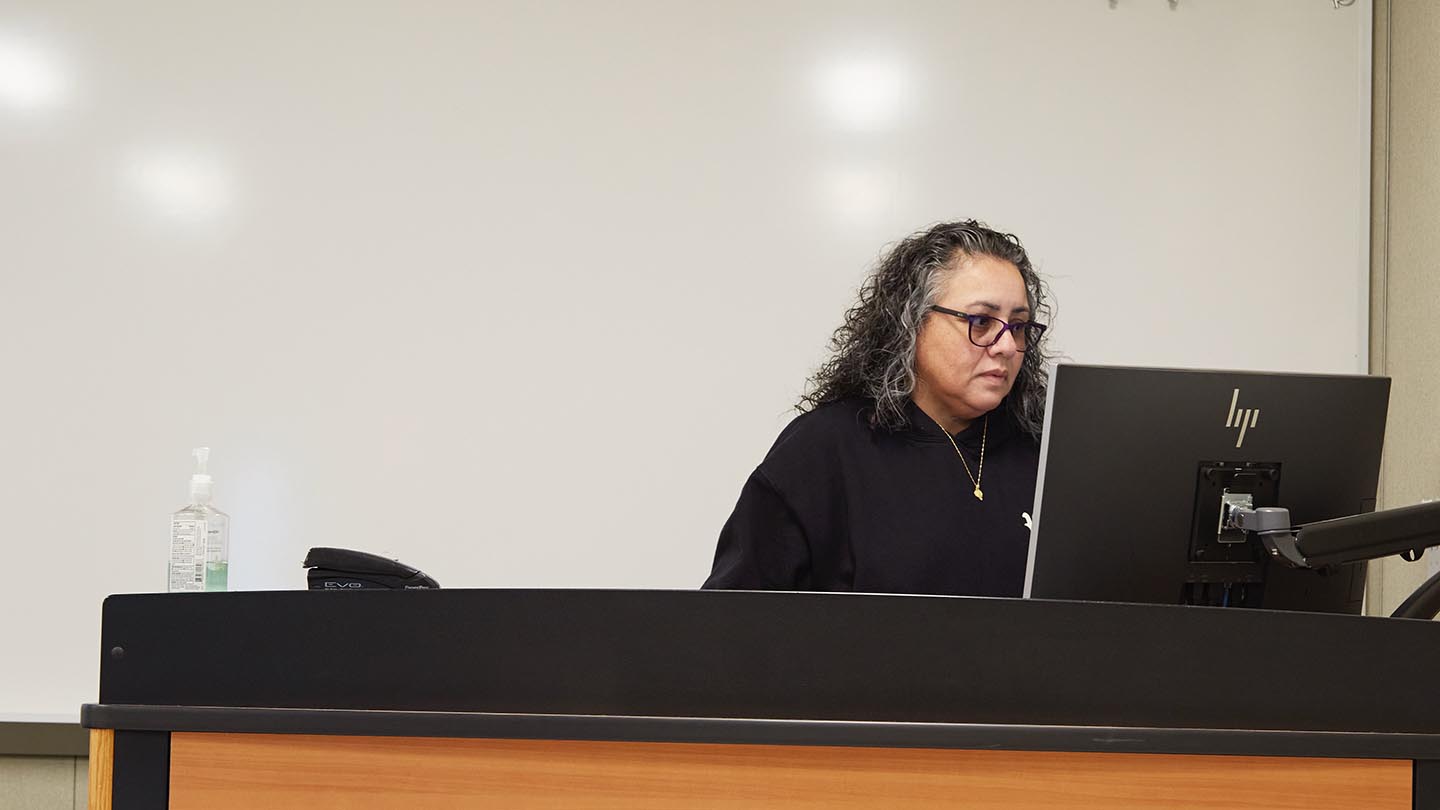 A female professor is prepping at the podium for her next lecture.