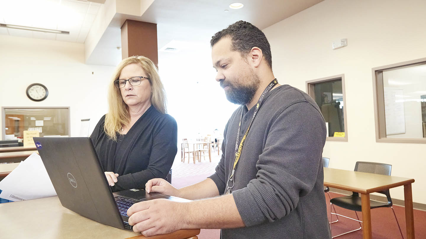 Male and female colleagues from the college staff review appointments on a laptop.