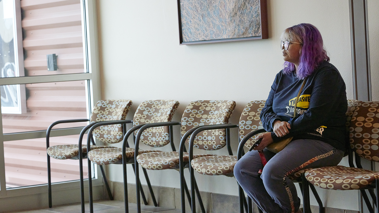 Female sits in empty row of seats along wall and gazes out a nearby window wall.